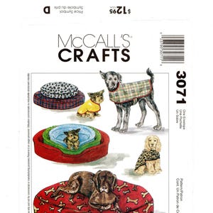 May include: McCall's Crafts pattern 3071. The image shows illustrations of dogs wearing coats and sitting on dog beds. The dog beds are red, blue, and green, with bone and leopard print patterns. The pattern includes one envelope.