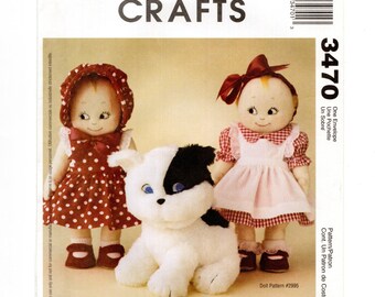 May include: McCall's Crafts doll pattern featuring two Kewpie dolls in dresses and a plush black and white dog. The dolls have painted faces and are wearing bonnets and bows. The pattern number is 3470.
