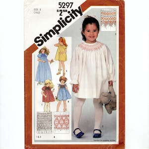May include: Simplicity pattern 5297 for child size 3. The cover features illustrations of several dresses, including a white dress with a smocked neckline. The price is $2.50. Transfers for smocking are included.