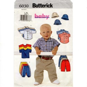 May include: A Butterick sewing pattern for baby clothes, featuring a smiling baby wearing a plaid shirt and khaki pants. The pattern includes various shirt styles, pants, and hats. The text "baby fashion essentials" is visible.