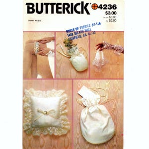 May include: A Butterick sewing pattern, number 4236, featuring various bridal accessories. The image includes a garter, a drawstring bag, a ring pillow, and lace gloves. The pattern is one size and includes the House of Fabrics address.