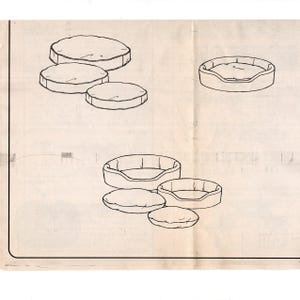 May include: Line drawing of pet beds and cushions. The image shows several variations of round pet beds with raised sides and matching round cushions. The beds and cushions are in different sizes, suggesting a pattern or design for pet accessories.