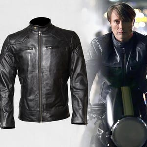 Può includere: Giacca da moto in pelle nera con collo alto, chiusura a zip e più tasche. La giacca presenta dettagli trapuntati sulle spalle e un classico stile biker. L'immagine mostra anche una persona che indossa una giacca simile in moto.