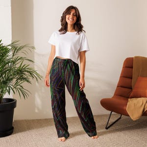May include: A woman in a white crop top and patterned pajama trousers. The trousers feature a dark base with green, purple, and red abstract lines. The trousers are loose-fitting and casual.