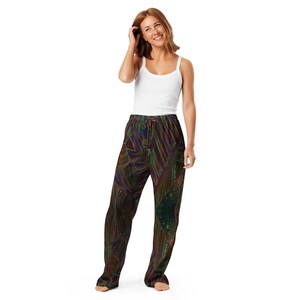 May include: A person wearing a white vest top and patterned pajama trousers. The pajama trousers feature a dark, abstract design with shades of green, red, and blue. The trousers have a drawstring waist and a relaxed fit.