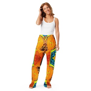 May include: A person wearing patterned pajama trousers with an abstract design. The trousers feature a vibrant mix of orange, yellow, blue, and green geometric and floral patterns. The person is also wearing a white vest top.
