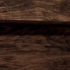 May include: Close-up of a section of dark brown wood with visible grain and texture. The wood appears to be a solid, sturdy material, possibly used for furniture or construction.