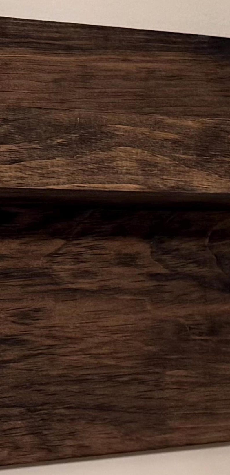 May include: Close-up of a section of dark brown wood with visible grain and texture. The wood appears to be a solid, sturdy material, possibly used for furniture or construction.