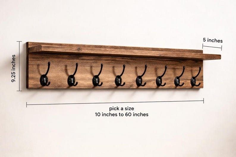 May include: A wooden wall-mounted coat rack with eight black metal hooks. The rack has a shelf and is 9.25 inches high and 5 inches deep. The length can be selected from 10 inches to 60 inches. The wood has a natural finish.