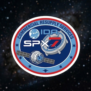 May include: A circular patch with the text "COMMERCIAL RESUPPLY SERVICES" in white lettering. The patch features a blue and red design with the letters "IDA" and "SPX" and an image of a satellite and a planet.
