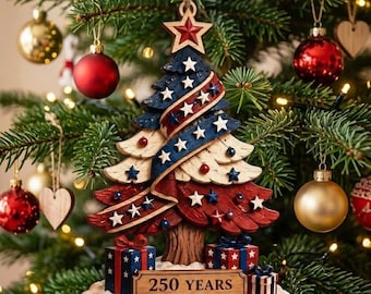 May include: A patriotic Christmas tree ornament featuring a layered design in red, white, and blue with star accents. The base includes two gift boxes and a wooden plaque with the text 250 YEARS 1776-2026, topped with a red star.