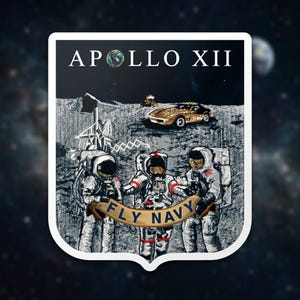 May include: A shield-shaped graphic featuring the words "APOLLO XII" above an illustration of astronauts on the moon. The image includes a gold car and the text "FLY NAVY" on a banner held by the astronauts.