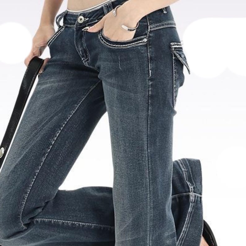 Puede incluir: Vaqueros de mezclilla azul oscuro con detalles de costuras blancas. Los vaqueros tienen un dise&ntilde;o cl&aacute;sico de cinco bolsillos, cierre de bot&oacute;n y cremallera, y un corte de pierna recta. El modelo lleva una pulsera plateada y sostiene un cintur&oacute;n negro.