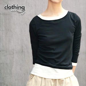 May include: Black long-sleeved top with a white neckline and cuffs, featuring a layered effect with a white under-layer. The text "clothing trend by Jose" is visible. The top is worn with beige trousers.