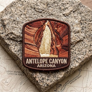 May include: A rectangular embroidered patch with rounded corners featuring a depiction of Antelope Canyon in shades of brown, orange, and cream. The text ANTELOPE CANYON ARIZONA is stitched in white capital letters at the bottom of the patch.
