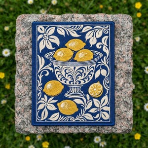 May include: A rectangular embroidered patch featuring a deep blue background with a central white decorative bowl filled with yellow lemons. The design is framed by white floral and leaf patterns, with additional lemons placed around the bowl.