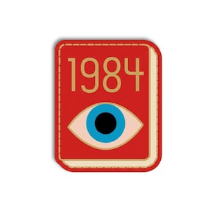 May include: A red rectangular pin with the gold text "1984" above a stylized eye with a blue iris and black pupil. The pin has a stitched border and a cream-colored spine.