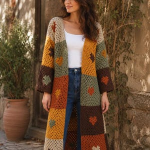 Puede incluir: Un cárdigan largo de ganchillo abierto por delante, hecho de parches cuadrados en tonos beige, amarillo mostaza, verde oliva y marrón oscuro. Cada cuadrado presenta un motivo en forma de corazón en contraste en el centro. Mangas largas y anchas.