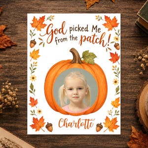 Peut inclure: Une carte rectangulaire illustrée d'une grande citrouille orange avec une découpe circulaire montrant la photographie d'une jeune enfant. Le texte indique God picked Me from the patch! et Charlotte. La bordure est ornée de feuilles d'automne et de glands.