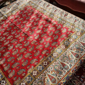 May include: A red area rug with a detailed paisley pattern. The rug features a central field of red with repeating paisley motifs in shades of blue, green, and gold. The border is a cream color with a larger paisley design.