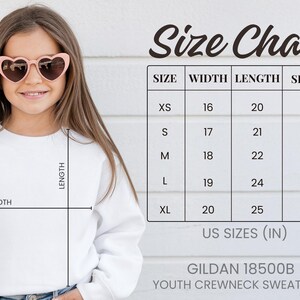 A young girl wearing a white crew neck sweatshirt and pink heart-shaped sunglasses, with a size chart and US sizes provided.