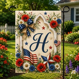 May include: A garden flag with patriotic design elements. The flag features a large blue letter "H", an American flag, red poppies, blue and white flowers, and a star-shaped design. A blue bow and a heart-shaped design with the American flag are also present.
