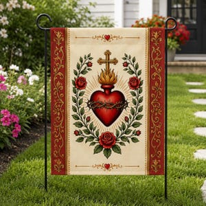 May include: A rectangular garden flag featuring a central red Sacred Heart encircled by a crown of thorns and topped with a golden cross and flames. The heart is framed by green rose vines with red blossoms on a cream background with red borders.