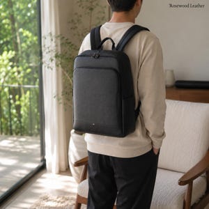 May include: A black backpack with a textured surface, a top handle, and two shoulder straps. The bag features a rectangular shape with a front zippered pocket and a main compartment. The text Rosewood Leather is visible in the top right corner.