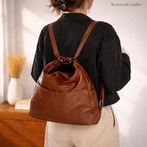 Könnte beinhalten: Ein brauner Lederrucksack mit zwei Vordertaschen und verstellbaren Trägern. Die Tasche wird auf dem Rücken getragen und hat einen oberen Griff. Der Text "Rosewood Leather" ist oben rechts sichtbar.