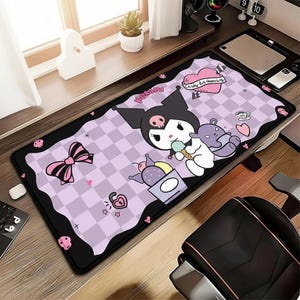 May include: A rectangular desk mouse mat with a cartoon character design. The mat has a black border and a light purple checkered background with pink accents, including a bow and hearts. The cartoon character is black and white and holding ice cream.