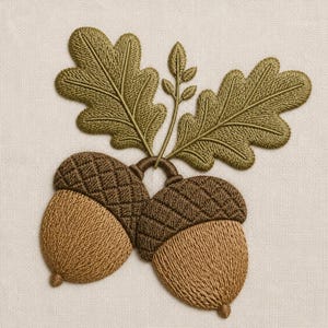 May include: An embroidered patch featuring two brown acorns with textured caps and light brown nuts, connected by a stem with two large, detailed olive green oak leaves and a small sprig of leaves extending upward, all on a light beige fabric.