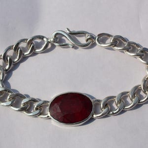 Puede incluir: Pulsera de plata con diseño de cadena de eslabones, con una gran gema de rubí rojo oscuro de corte ovalado. El rubí está engastado en un bisel de plata. La pulsera tiene un cierre seguro.