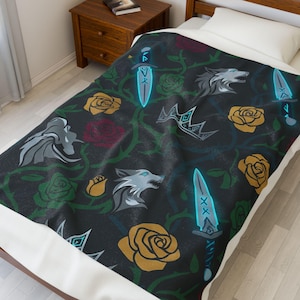 May include: A black blanket with a repeating pattern of stylized wolves, daggers, crowns, and roses in shades of gray, yellow, and red. The design includes green vines and thorns. The blanket is on a bed with a white sheet.