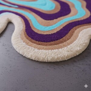 Op de afbeelding: Een golvend, abstract tapijt met een cr&egrave;mekleurige rand en een patroon van wervelende strepen. De strepen hebben tinten paars, bruin en blauwgroen. Het tapijt heeft een zacht, getextureerd uiterlijk, wat een comfortabele vloerbedekking suggereert.