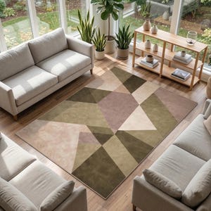May include: A geometric patterned area rug in shades of olive green, beige, and blush pink. The rug is placed on a hardwood floor, surrounded by light-colored sofas and potted plants. The room has large windows.