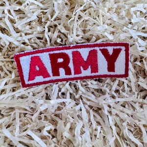 May include: A rectangular patch with the word "ARMY" in bold red letters on a white background, framed by a red border. The patch is set against a background of shredded paper.