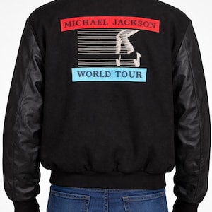 Puede incluir: Chaqueta negra con mangas de cuero. La parte trasera presenta un gráfico con el texto "MICHAEL JACKSON" en rojo y "WORLD TOUR" en azul. La chaqueta tiene dobladillo y puños acanalados.