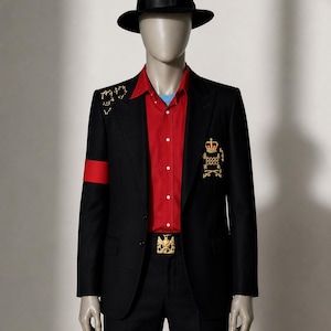 May include: A black suit with gold detailing, a red armband, and a red shirt. The outfit includes a black fedora hat and a gold buckle belt. The suit is displayed on a mannequin.