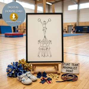 May include: A black and white line art print in a black frame depicting a cheerleading stunt team. The print shows four figures in a pyramid formation. Below the frame are blue and gold pom-poms, white trainers, hair bows, and a ribbon.