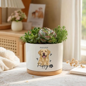 May include: A white ceramic cylindrical planter with a wooden base, containing various green succulents. The front features a graphic of a golden retriever, the text 2016-2026, the word Puppy, small heart icons, and a black paw print graphic.