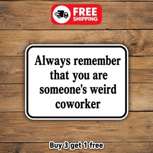 May include: A white rectangular sticker with rounded corners, featuring the text "Always remember that you are someone's weird coworker" in black. A red banner with "FREE SHIPPING" is in the top right corner. The sticker is on a wooden background.