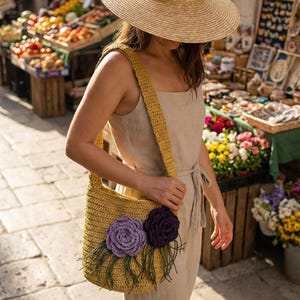 May include: A straw sun hat and a yellow crocheted shoulder bag with purple and dark purple flower accents. The bag has a long strap and is carried by a person wearing a beige jumpsuit. The background shows a market with produce and flowers.