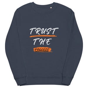 Puede incluir: Sudadera azul marino con la frase "TRUST THE PROCESS" en escritura blanca y detalles en naranja. La sudadera tiene cuello redondo y mangas largas. El texto está centrado en el pecho.
