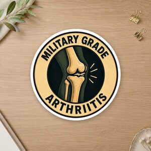 May include: A circular sticker with a cream-colored border and a dark green center. The text MILITARY GRADE ARTHRITIS is printed in black capital letters around the edge. The center features a detailed illustration of a human knee joint.
