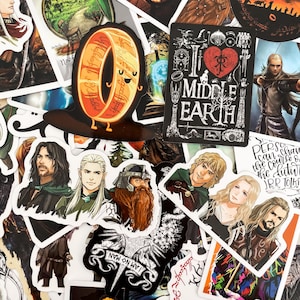 Può includere: Una collezione di adesivi con personaggi e simboli de Il Signore degli Anelli. Include immagini dell'Unico Anello, la frase "I love Middle Earth" e vari personaggi come Aragorn e Legolas.