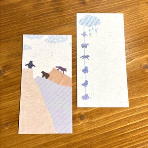 May include: Two rectangular paper cards with animal illustrations. One card features a penguin, bear, and fox on a mountain scene. The other card has a series of animal silhouettes hanging from a cloud.