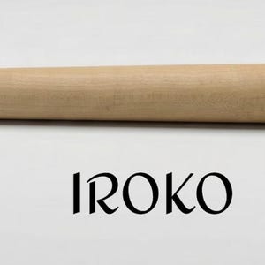 Op de afbeelding: Een gladde, lichtgekleurde houten doorn met een taps toelopende cilindrische vorm. Onder het houten object staat het woord IROKO gedrukt in een zwart, gestileerd schreeflettertype tegen een neutrale achtergrond. Het object is lang en recht.
