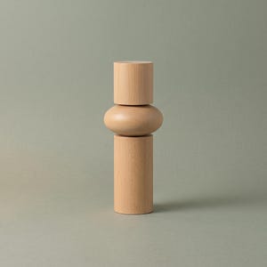 May include: A light-colored wooden object composed of three stacked geometric shapes. The base is a tall cylinder, the middle section is a rounded, flattened sphere, and the top is a smaller cylinder, all featuring a smooth, natural wood grain finish.