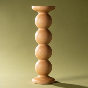 May include: A light-coloured wooden candle holder featuring a vertical stack of four smooth, spherical shapes. The object has a wide, flat circular base and a matching flat circular top, showcasing a natural wood grain pattern throughout its surface.