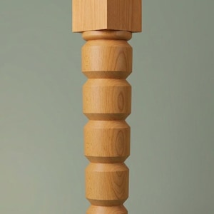 Peut inclure: Un pied de meuble en bois brun clair doté d'un bloc supérieur carré qui se transforme en une série de cinq segments cylindriques empilés, arrondis et facettés, se terminant par une base circulaire lisse et plate au bas de la colonne.